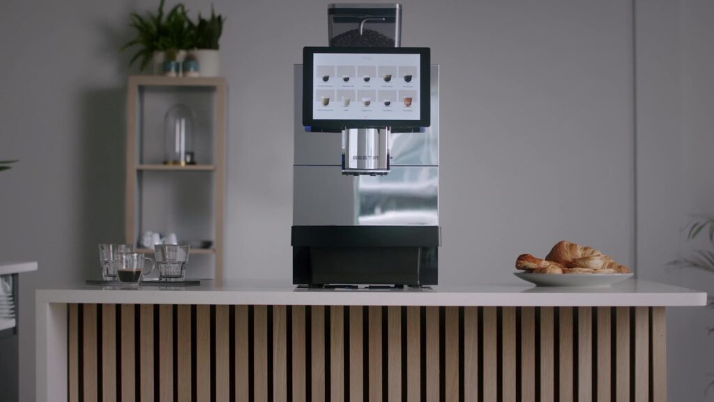 Bestir BM80 bean-to-cup coffee machine on a modern office counter with a touchscreen menu, coffee cups and pastries.